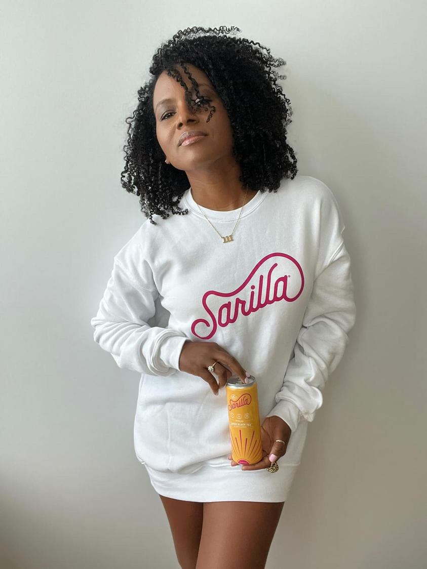 Faith holding one of our lemon spritzers and posing a cozy white Sarilla sweatshirt, styled for a relaxed fit. The image captures the soft texture and versatile design, perfect for everyday comfort